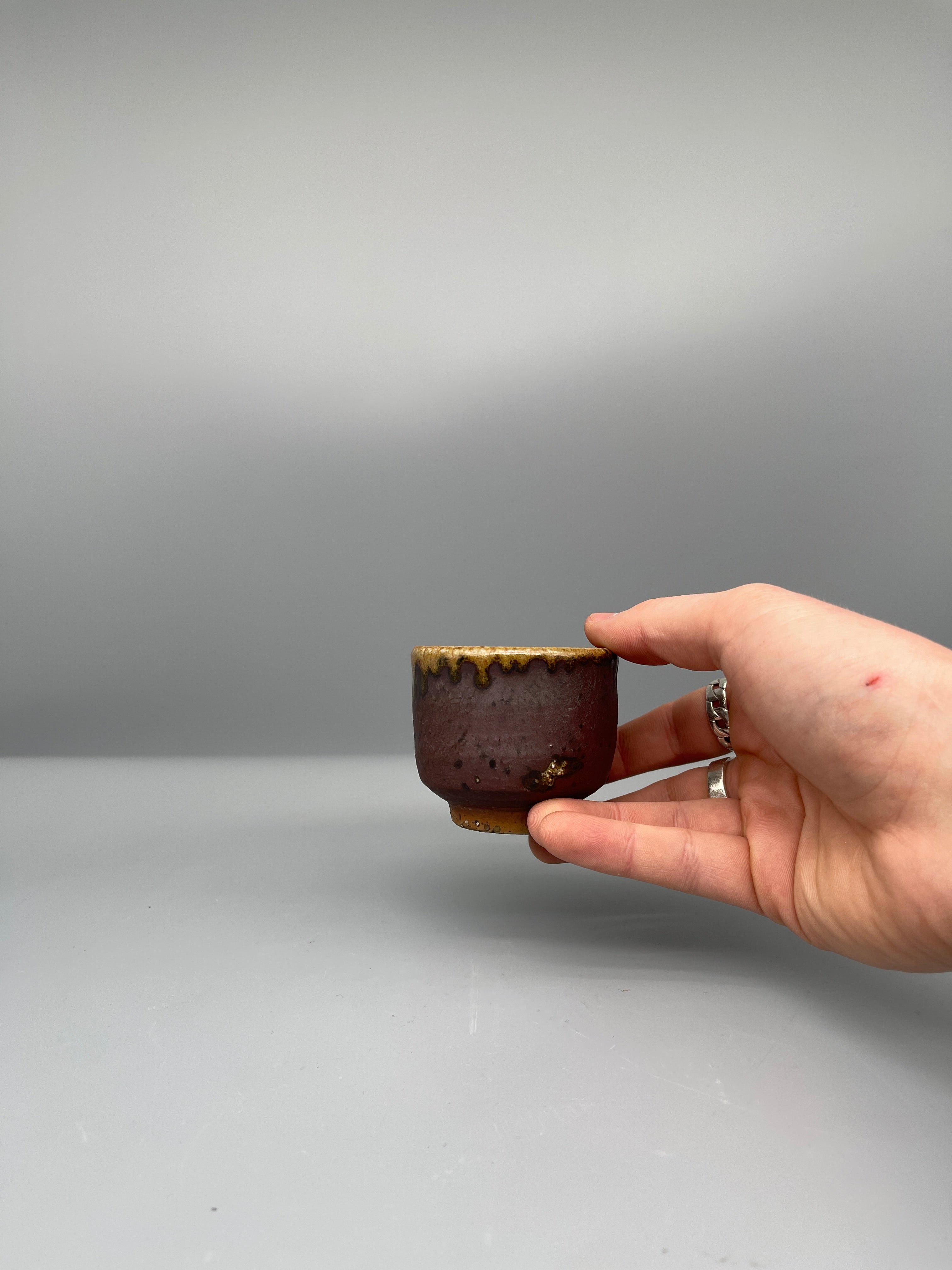 Vintage Japanese bizen guinomi cup, plum brown, held for scale